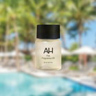 A small bottle of fragrance oil with the label 'AH The Fragrance Oil', set against a blurred background depicting a pool and palm trees.