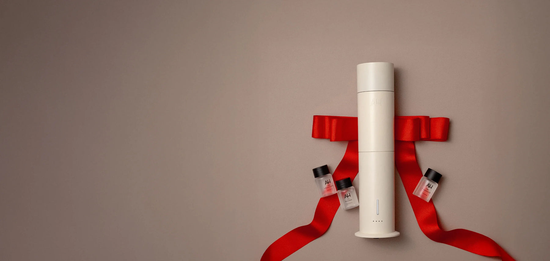 White cylindrical product with smaller bottles and a red ribbon on a beige background